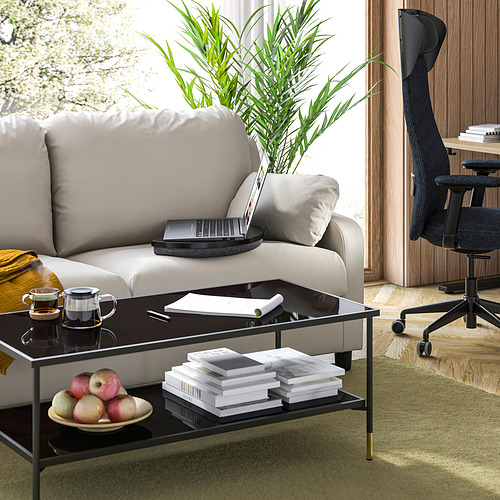 Sala de estar moderna con sofá gris, bandeja negra para computadora portátil, alfombra verde y piso de madera.