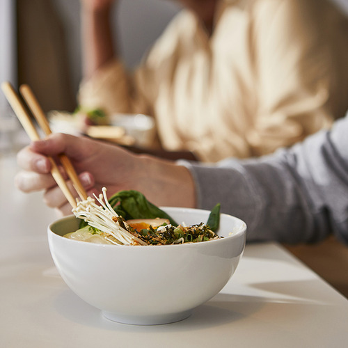 Persona que sostiene palillos sobre un plato de sopa de verduras sobre una mesa.