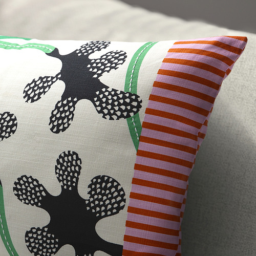 Un cojín con grandes motivos florales negros y rayas verticales brillantes en rosa y naranja en un lado, que descansa sobre una superficie de color claro.
