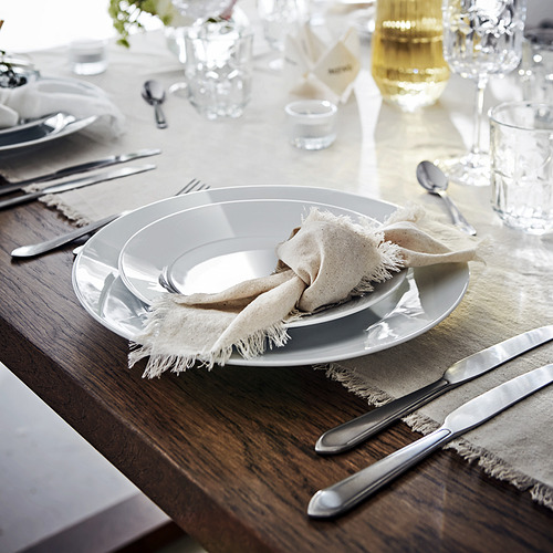 Mesa con platos, cubiertos y vasos de porcelana blanca. Colocado sobre una mesa de madera con servilletas de tela beige.