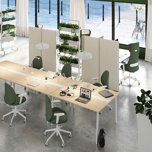 Moderna configuración de oficina con mesas beige MITTZON, sillas verdes y divisores altos. Portátiles y lámparas sobre mesas, grandes ventanales al fondo.