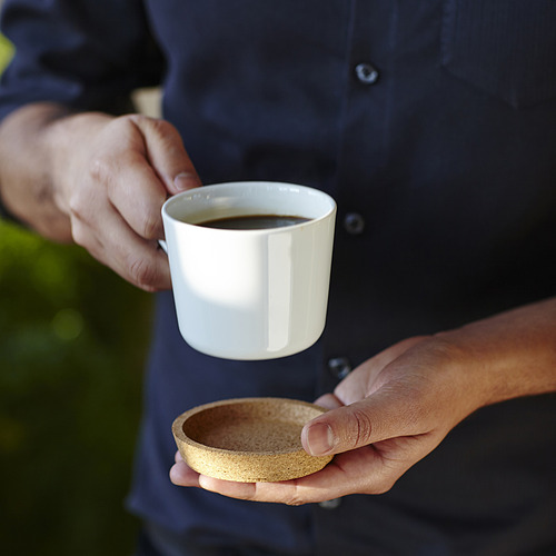 Persona sosteniendo una taza blanca con café y otro plato pequeño.