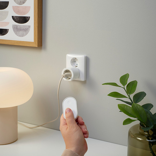 Conecta a mano una lámpara inteligente a un enchufe de pared, junto a una planta y una lámpara de arte.