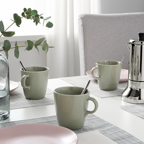 Dos tazas con cucharas sobre un mantel de mesa, junto a una jarra de agua y una cafetera, que indican la preparación para servir el café o el té.