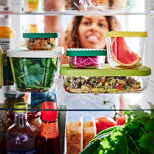 Nevera con contenedores HAVSTOBIS en verde y amarillo que almacena ensaladas, verduras y sobras. Cuidadosamente apilados, ahorrando espacio y manteniendo los alimentos frescos.
