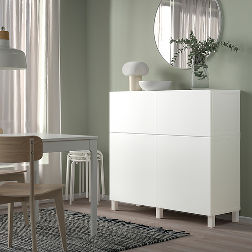 Un mueble alto y blanco de IKEA BESTÅ con cuatro puertas, situado en una zona de comedor con decoración en la parte superior.
