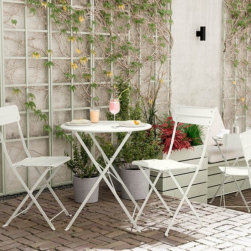 Acogedora escena de balcón con mesa SUNDSÖ blanca y sillas plegables, rodeada de plantas en macetas.