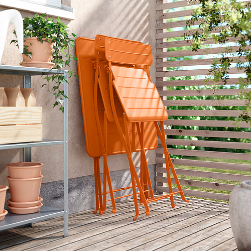 Tres sillas metálicas SUNDSÖ naranjas apiladas. Ideal para espacios exteriores, duradero y fácil de almacenar.