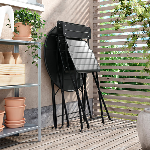 Sillas metálicas plegables negras, apiladas sobre cubierta de madera, ideales para balcones con diseño moderno.