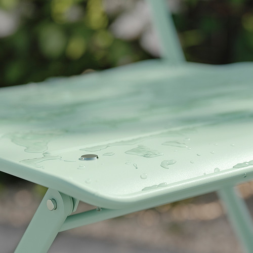 Silla de metal verde claro con gotas de agua en el asiento.