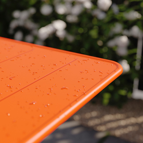 Superficie de mesa plegable de color naranja brillante con gotas de agua, colocada al aire libre.