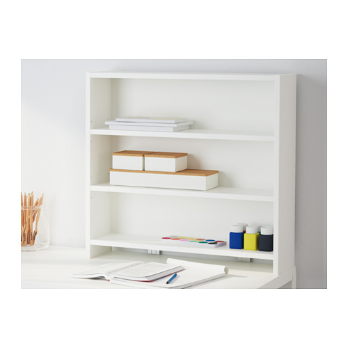 Un escritorio blanco con almacenamiento en el estante superior. Sostiene libros, papeles y materiales de arte de manera ordenada.