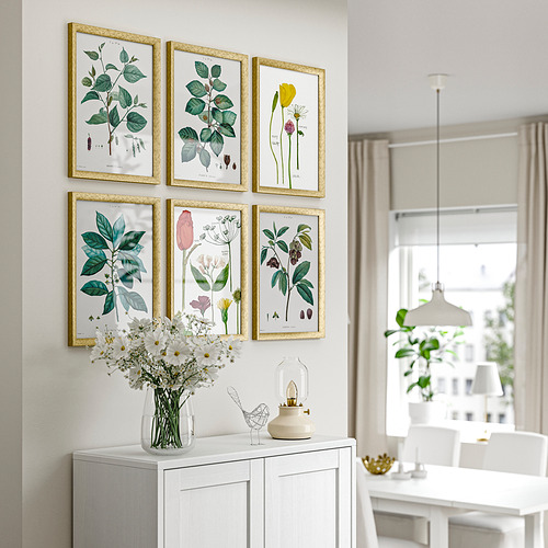 Seis estampados florales con marco dorado en la pared, flores blancas en jarrón transparente, lámpara blanca en la consola debajo.