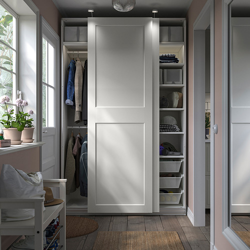 Moderno armario blanco con puertas correderas, estantes y espacio para colgar. Incluye una silla, plantas y piso de madera.