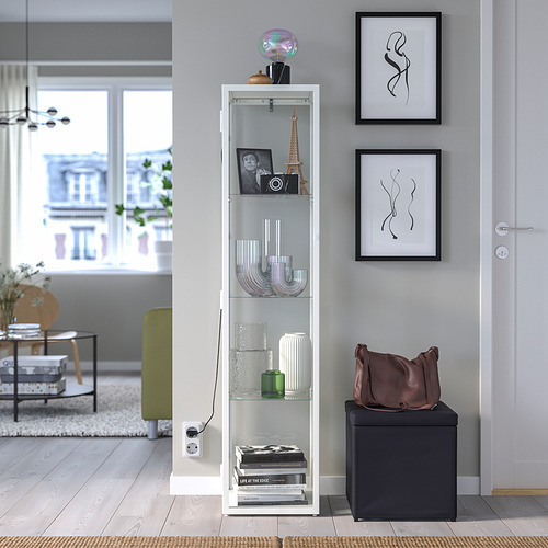 Sala de estar moderna con mueble blanco BLÅLIDEN, estantes decorados, marcos de arte y otomana oscura.