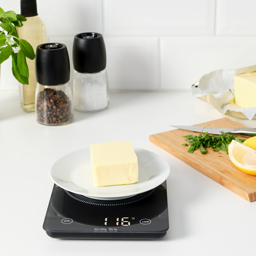 Báscula de cocina digital negra con plato blanco y mantequilla; Pantalla LED, hierbas picadas, limón y cuchillo cerca.