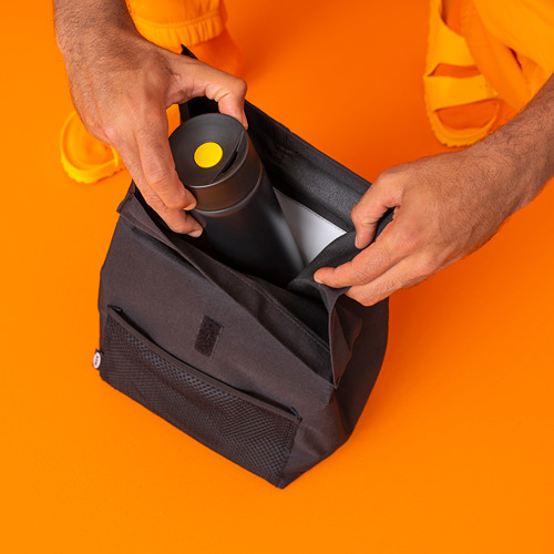 Persona colocando una bolsa de almuerzo aislada negra en una bolsa naranja.