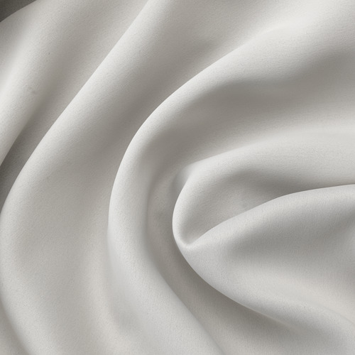 Cortinas blancas plegadas de cerca, textura suave, mostrando tela de calidad.