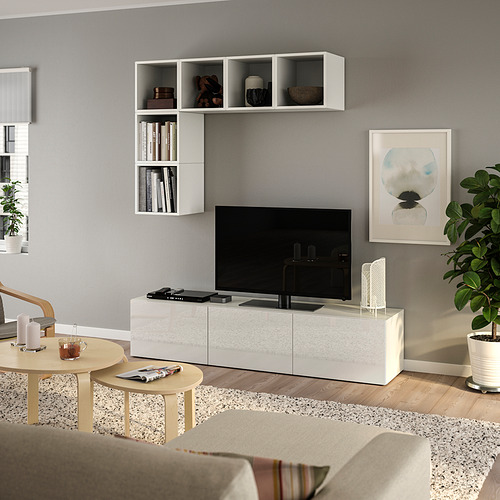 Sala de estar moderna con banco de TV blanco BESTÅ, TV de pantalla plana, estantes abiertos, obras de arte, plantas y mesa de centro circular.