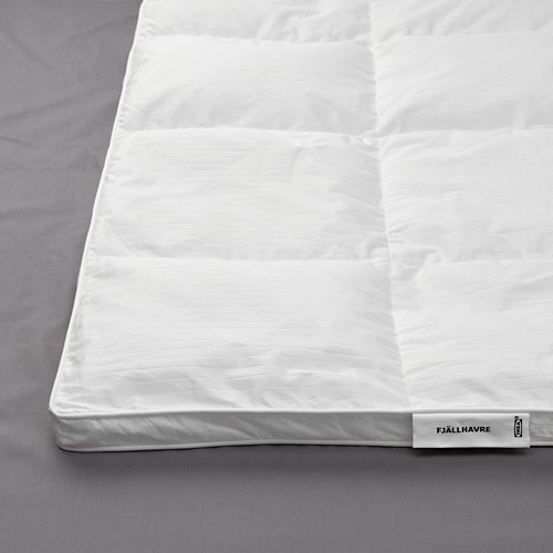 Un edredón fjällräven blanco de felpa expuesto sobre una cama, con lados cosidos para mayor calidez, lo que indica comodidad de alta calidad y materiales lujosos.