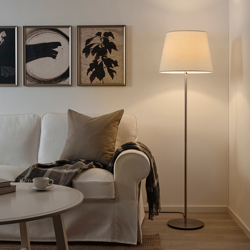 Acogedor rincón de la sala de estar con lámpara, silla, taza, libro y arte abstracto SKAFTET.