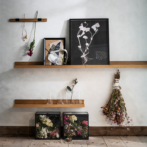 Estantes montados en la pared con marco de bambú que muestran varios artículos decorativos que incluyen flores, impresiones artísticas y jarrones.