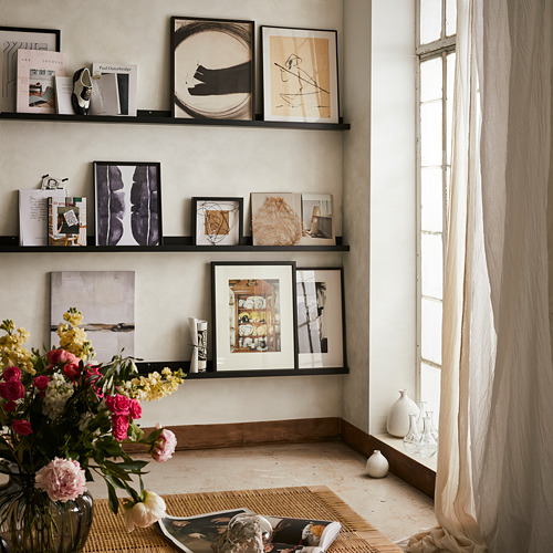 Habitación moderna con repisas de cuadros negros MOSSLANDA que muestran arte abstracto y flores vibrantes cerca de una ventana.