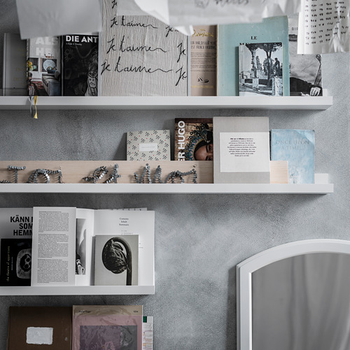Estantes blancos con libros, fotos y decoración. Algunos libros se abren, imágenes en blanco y negro.
