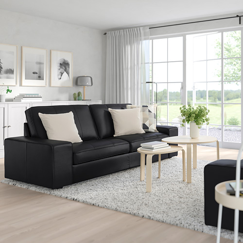 Moderno salón con gran sofá negro KIVIK, cojines blancos, mesa de centro de madera y grandes ventanales. Decoración luminosa, minimalista y con luz natural.
