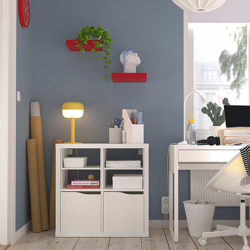 Oficina en casa con estante KALLAX, libros, lámpara brillante, estantes de plantas rojas, reloj, escritorio, computadora. Pared azul, suelo de madera.