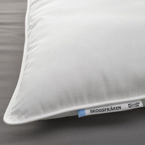 Primer plano de una almohada blanca de IKEA SKOGSFRÄKEN sobre una cama, mostrando su tela suave y de soporte, y la etiqueta de marca en la esquina.