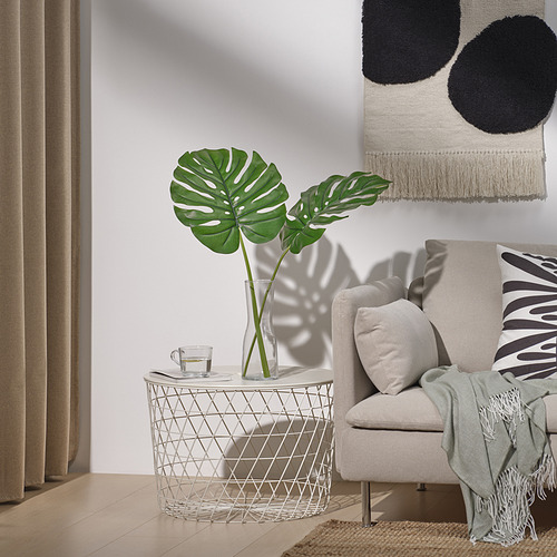 Sala de estar moderna con hoja verde en jarrón, silla, manta, cortinas, arte de pared, piso de madera y taza de té.