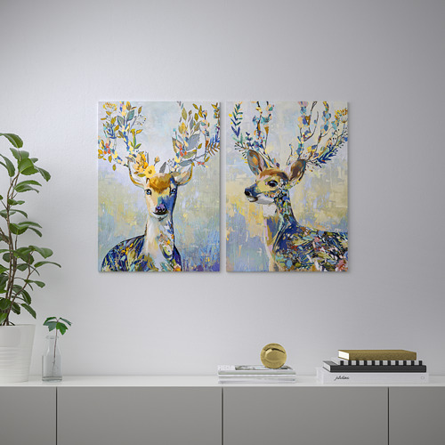 Dos vibrantes pinturas de ciervos con cuernos florales cuelgan de una pared sobre un estante gris. La estantería contiene varios elementos decorativos.