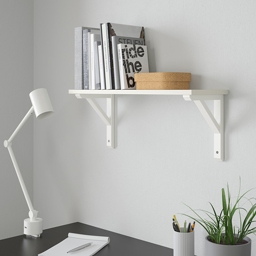 Estante de pared blanco minimalista - BURHULT, contiene libros, caja pequeña, montado en la pared sobre el escritorio. Lámpara y planta al lado. Estantería pequeña, libros más altos.