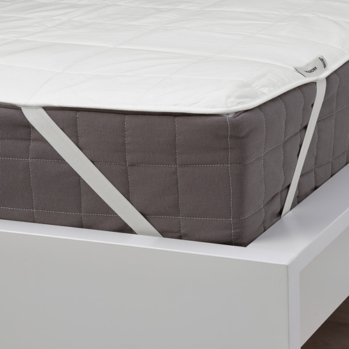 Un protector de colchón blanco acolchado sobre una cama, asegurado con correas elásticas, que protege y prolonga la vida útil del colchón.
