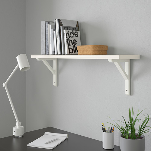 Estantería blanca con libros y caja, escritorio con bloc de notas, lámpara, bolígrafos, planta.