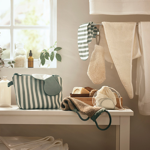 Escena de baño con bolso de rayas verdes/blancas, toallas blancas y toalla para el cabello colgante. Ventana con planta.