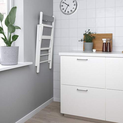 Cocina moderna con asiento de escalera plegable y paredes grises. Armarios blancos, planta en maceta y reloj.