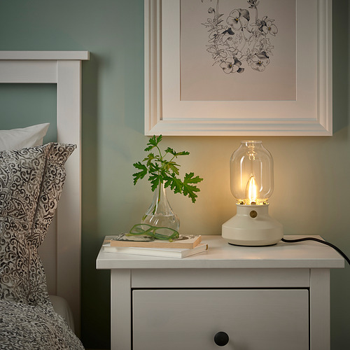 Dormitorio con lámpara LUNNOM, estampado floral, y cama con almohada y libros.