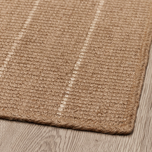 Felpudo de yute con bordes trenzados, cuidadosamente colocado sobre un suelo de madera, que muestra un tejido intrincado y una textura natural.