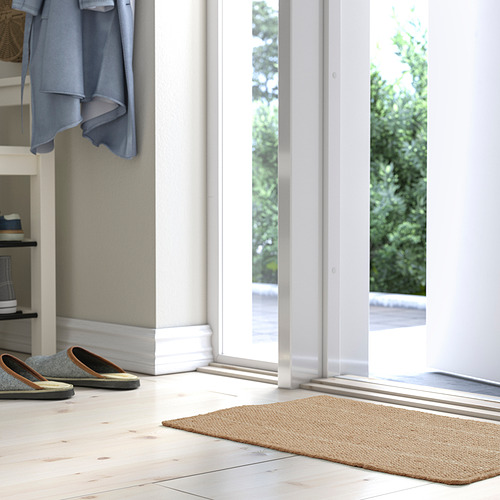 Entrada luminosa con alfombra TIOKRONA beige, chaqueta azul, diseño limpio.