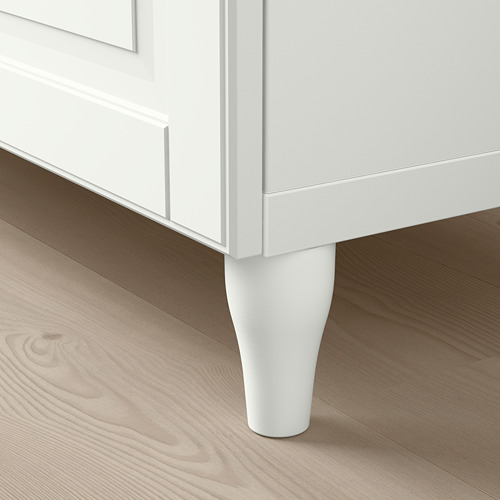 Un elegante armario blanco BESTÅ con una pata cónica se apoya en suelos de madera clara, mostrando sus líneas limpias y su diseño moderno.