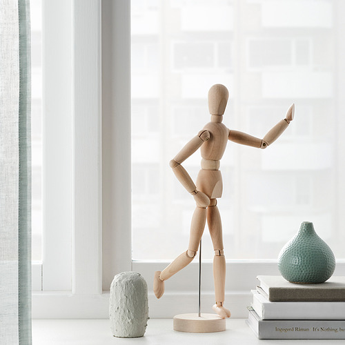 Expositores de maniquíes de artista de madera, colocados cerca de una ventana, rodeados de jarrones decorativos y libros.