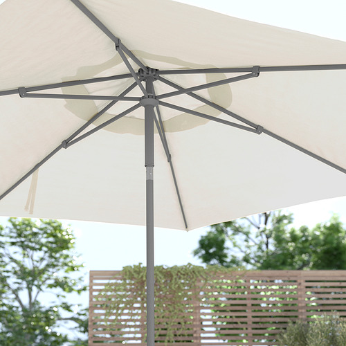 Describir JOGGESÖ sombrilla de patio beige con poste de aluminio y costillas de acero, inclinada para dar sombra.
