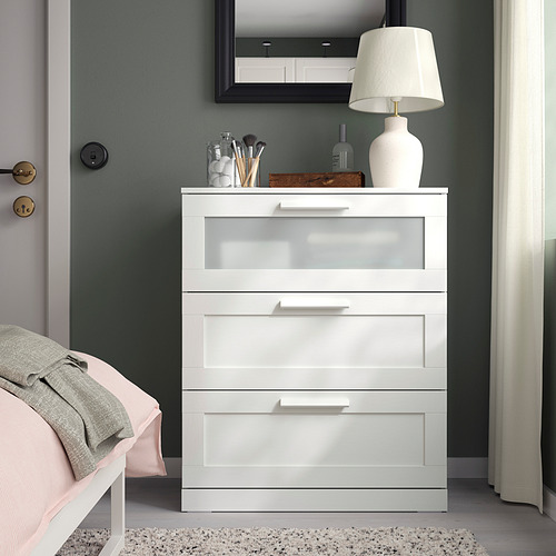 Baúl blanco BRIMNES con cajón de cristal, espejo, lámpara y cama en la habitación.