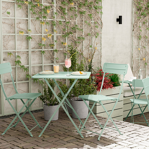 Escena al aire libre con mesa y sillas de metal turquesa SUNDSÖ, plantas en macetas, set para comer.
