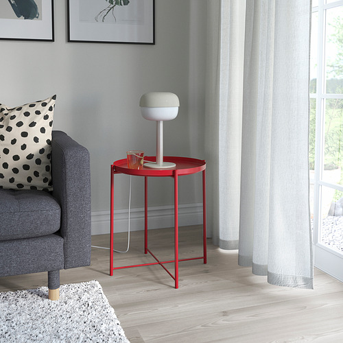 Lámpara BLÅSVERK blanca moderna en pie rojo junto a la silla de lunares cerca de la ventana.