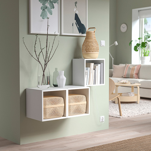 Sala de estar minimalista con almacenamiento EKET, cajas de mimbre, jarrones, libros, plantas, arte y sofá.