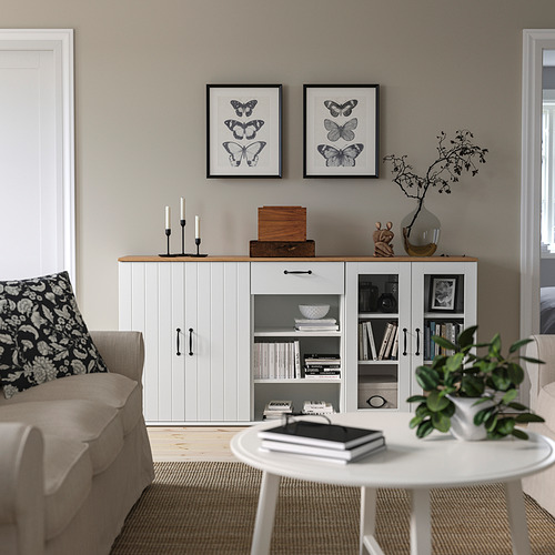 Sala de estar moderna con aparador SKRUVBY, estampados de mariposas, sofá beige y mesa de centro redonda con libros y plantas.