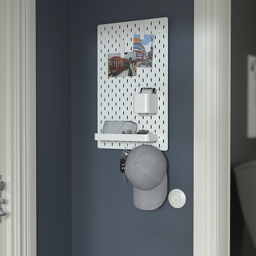 Un tablero perforado SKÅDIS montado en la pared organiza artículos como llaves, billetera y sombrero. Incluye un portavasos y un estante de almacenamiento.
